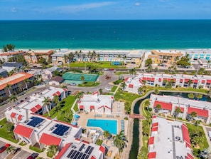 Um resort com piscina, quadra de tênis e vista para a praia.