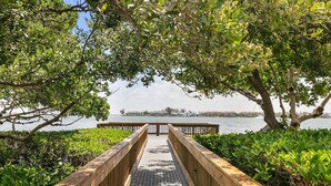 A wooden boardwalk leading to a waterfront with dense foliage overhead. - Endless Memories - 1801   “Anna Maria Island” (Bradenton Beach)