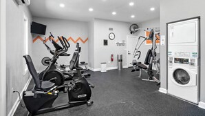 A gym with cardio machines, a wall-mounted TV, a clock, and a washing machine. - Endless Memories - 1801   “Anna Maria Island” (Bradenton Beach)