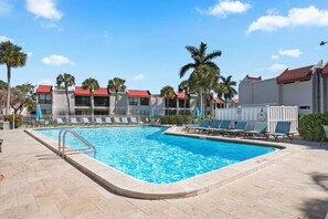 Uma piscina com espreguiçadeiras, palmeiras e um edifício com telhados vermelhos.