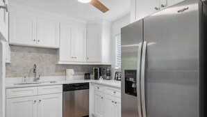 A modern kitchen with white cabinets, a stainless steel refrigerator, a dishwasher, and a built-in coffee maker. - Endless Memories - 1801   “Anna Maria Island” (Bradenton Beach)
