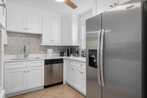 A modern kitchen with white cabinets, a stainless steel refrigerator, a dishwasher, and a built-in coffee maker. - Endless Memories - 1801   “Anna Maria Island” (Bradenton Beach)