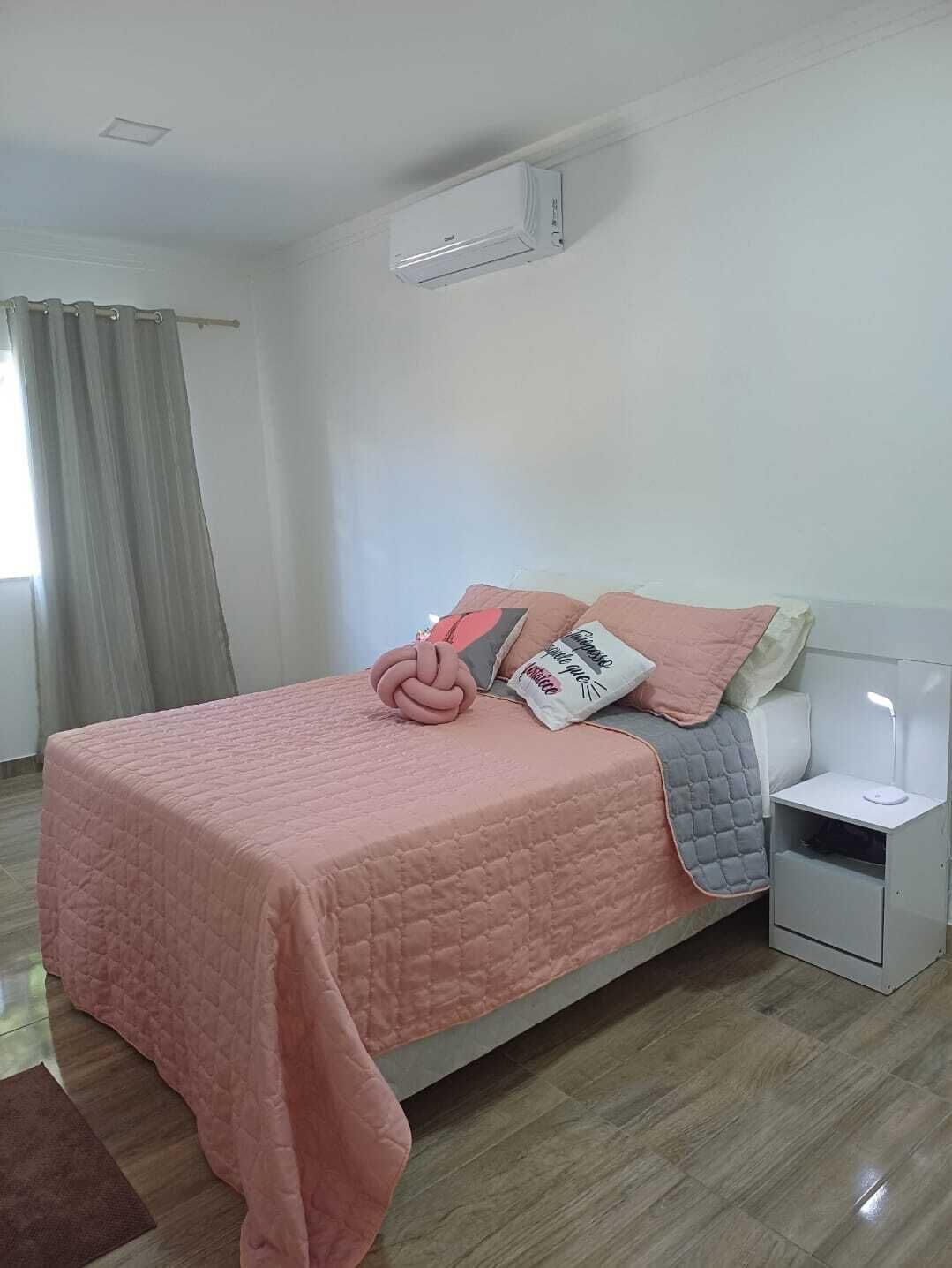 A neatly made bed with a pink quilt, a bedside lamp, and a small bedside table.