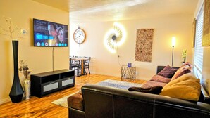 Een woonkamer met een televisie, een klok, een wandlamp en een bank.