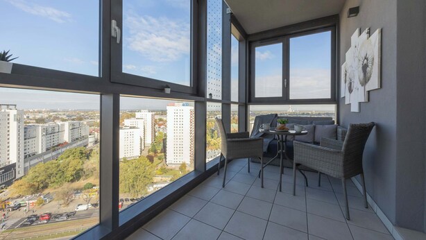 A balcony with a view of a cityscape, a seating area with a table and chairs, and artwork on the wall.