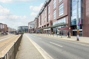 A street with a tram track, buildings, and pedestrians.