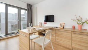 A modern, well-lit room with a large window, a flat-screen TV, a wooden dining table, white chairs, and a minimalist decor. - Stylish Studio in the Center | Air Conditioning | Parking (Wrocław)