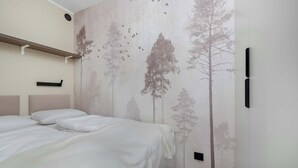 A bedroom with a bed, a headboard, a wall-mounted shelf, and a wall with a tree and bird mural.