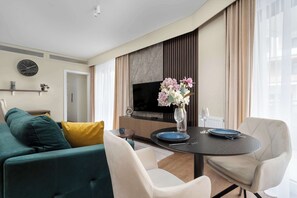 A modern living room with a sofa, chairs, a dining table, a TV, and a vase with flowers.
