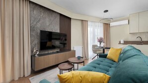 A modern living room with a large flat-screen TV, a teal sofa, yellow cushions, a wooden sideboard, and a small round table.