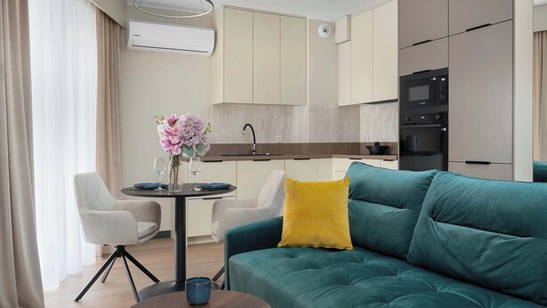 A modern living room with a teal sofa, a yellow pillow, and a dining area with a table and chairs.