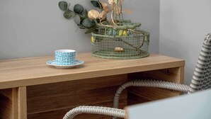 A wooden table with a decorative birdcage, a patterned cup, and a plant.