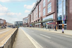 A street with tram tracks, modern buildings, and pedestrians.