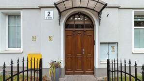 A building with a double wooden door, a number '2' sign, a yellow mailbox, and a black iron fence.