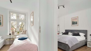 A bedroom with a bed, a bedside table, a window, and a door.