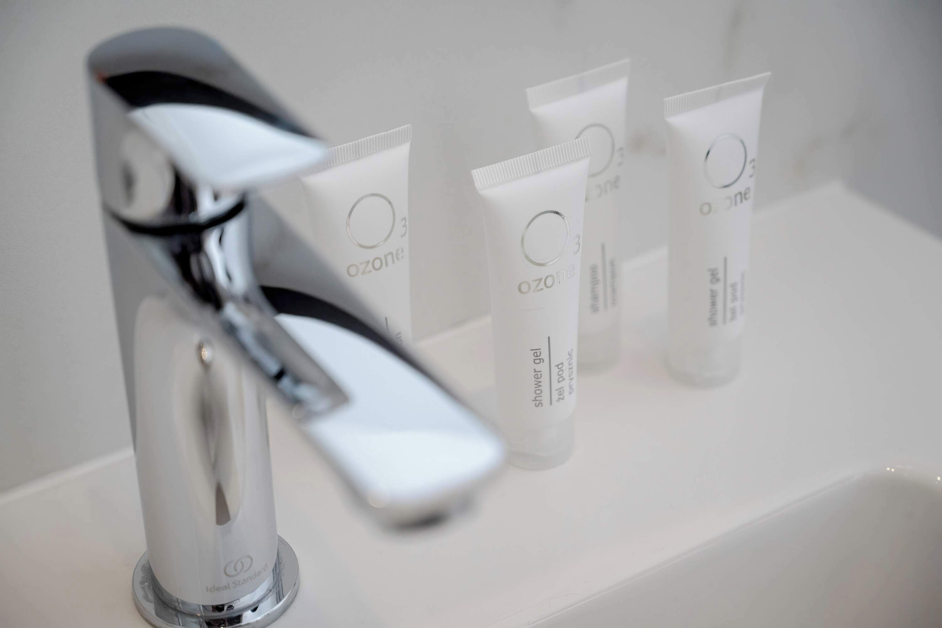 Ein Badezimmer mit einem modernen Chromarmaturen und drei Tubes Ozons Duschgel auf einem weißen Waschbecken.