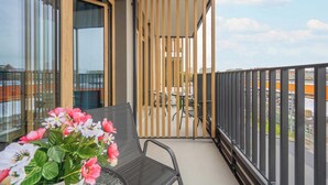 A balcony with a view of a cityscape, a table with chairs, and a potted plant with flowers.