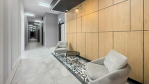 A modern hallway with a patterned carpet, two armchairs, a round table, and a wooden wall with a geometric light fixture.