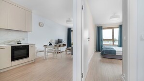 A modern kitchen with a built-in oven, a dining area with a table and chairs, and a bedroom with a bed and curtains.