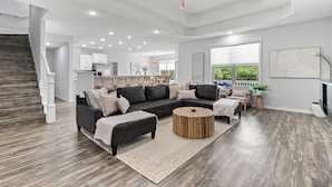 A spacious living area with a dark-colored sectional sofa, a round wooden coffee table, and a staircase with wooden railings. - 30a Tropical Breeze Beach Home Near Beach! 6Seater Lsv, Pool, Gated Community (Santa Rosa Beach)