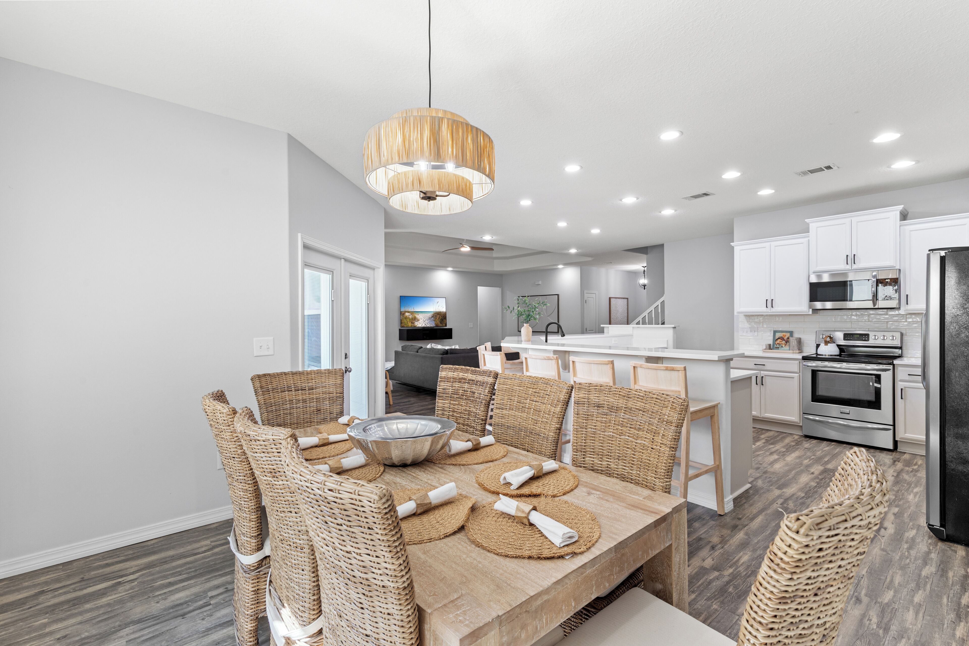A modern kitchen with white cabinets, stainless steel appliances, and a dining area with wicker chairs and a wooden table.
