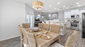 A modern kitchen with white cabinets, stainless steel appliances, and a dining area with wicker chairs and a wooden table. - 30a Tropical Breeze Beach Home Near Beach! 6Seater Lsv, Pool, Gated Community (Santa Rosa Beach)