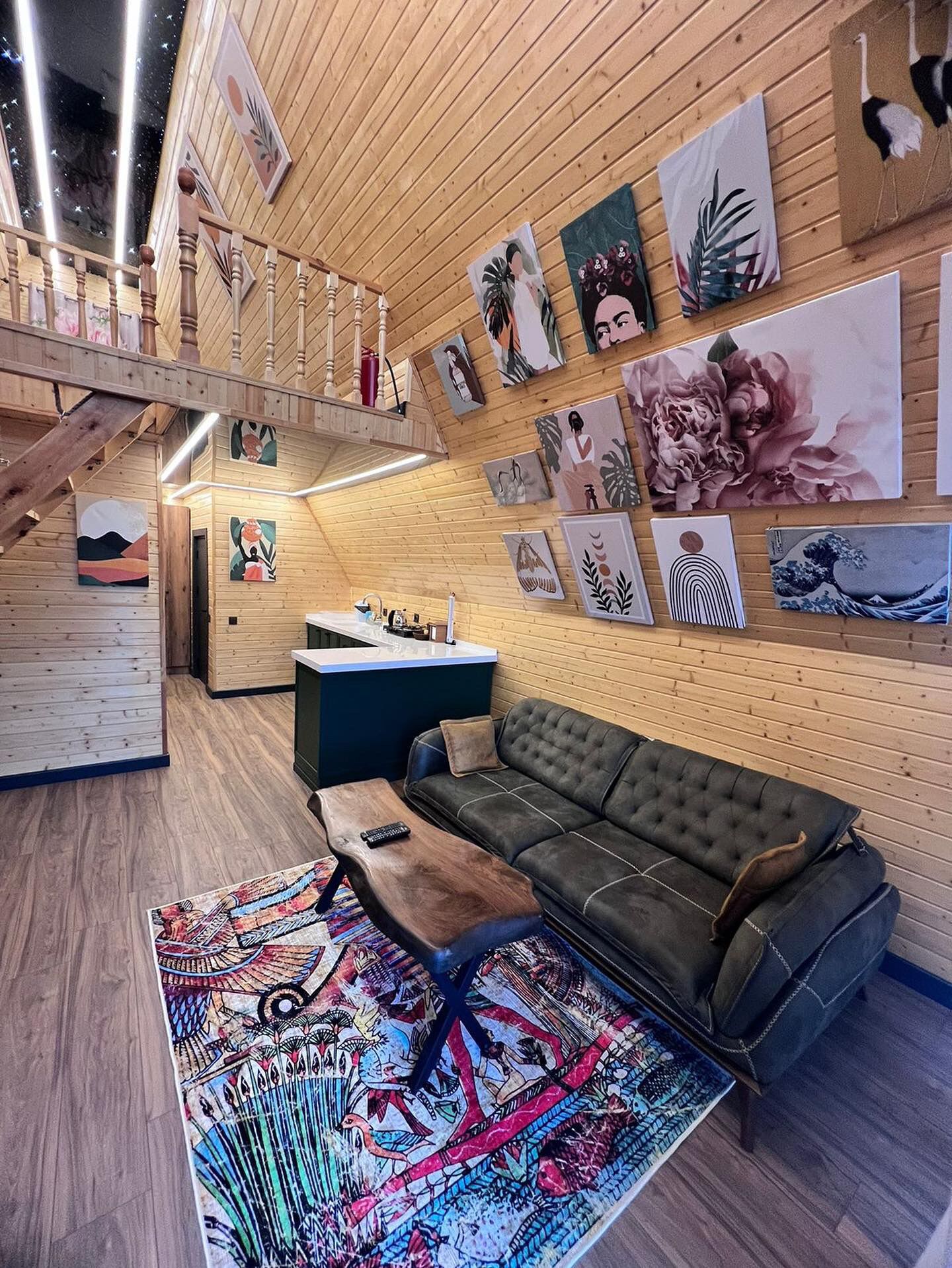 Un intérieur chaleureux avec un escalier en bois, un canapé, une table basse et diverses œuvres d’art accrochées aux murs.