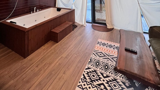 A modern, sloped-roofed room with a wooden interior, a large window with curtains, a built-in bathtub, and a flat-screen TV mounted on the wall. - Dekoriza Glamping  (Ismailli)