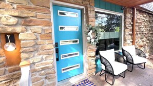 Fachada de piedra con puerta azul, asientos exteriores y un pequeño porche.