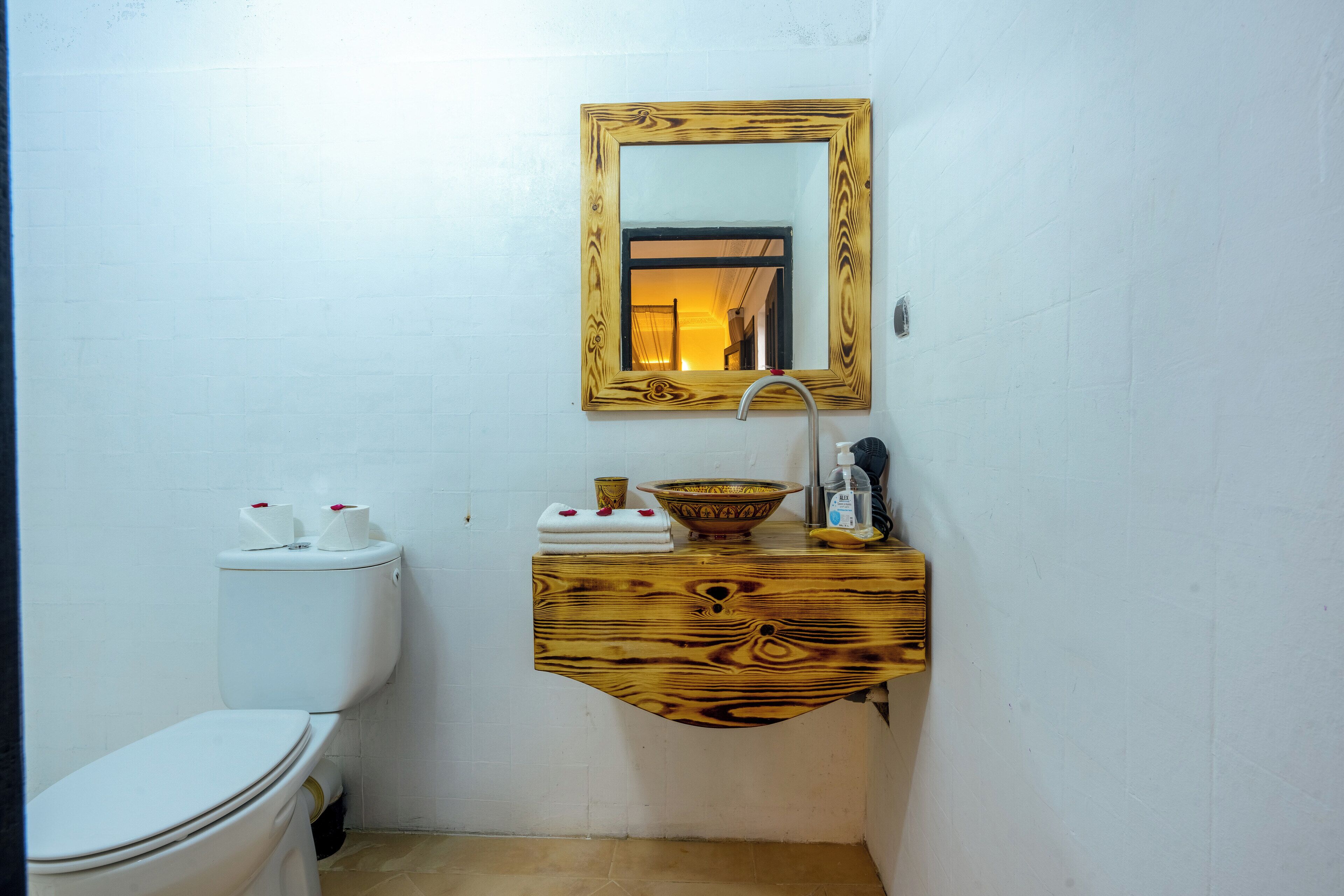 A small bathroom with a white toilet, a wooden vanity with a mirror, and a sink.