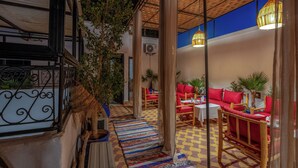 Un espace extérieur aménagé avec des chaises rouges et un sol à carreaux, entouré de plantes et surmonté d’un toit de chaume.