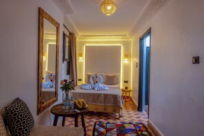 A hotel room with a bed, a mirror, a small table with a vase and bananas, and a colorful rug. - Riad des Remparts  (Marrakech)
