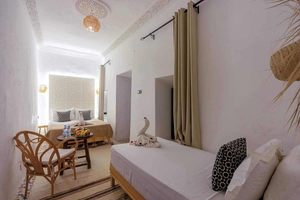 A hotel room with a bed, a dining area with a table and chairs, a decorative swan on the bed, and a view of the outside.