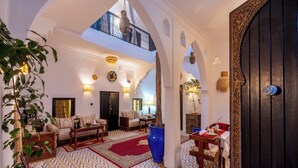 Un vaste espace de vie doté d’un plafond haut, un coin repas avec une nappe rouge et un grand vase bleu.