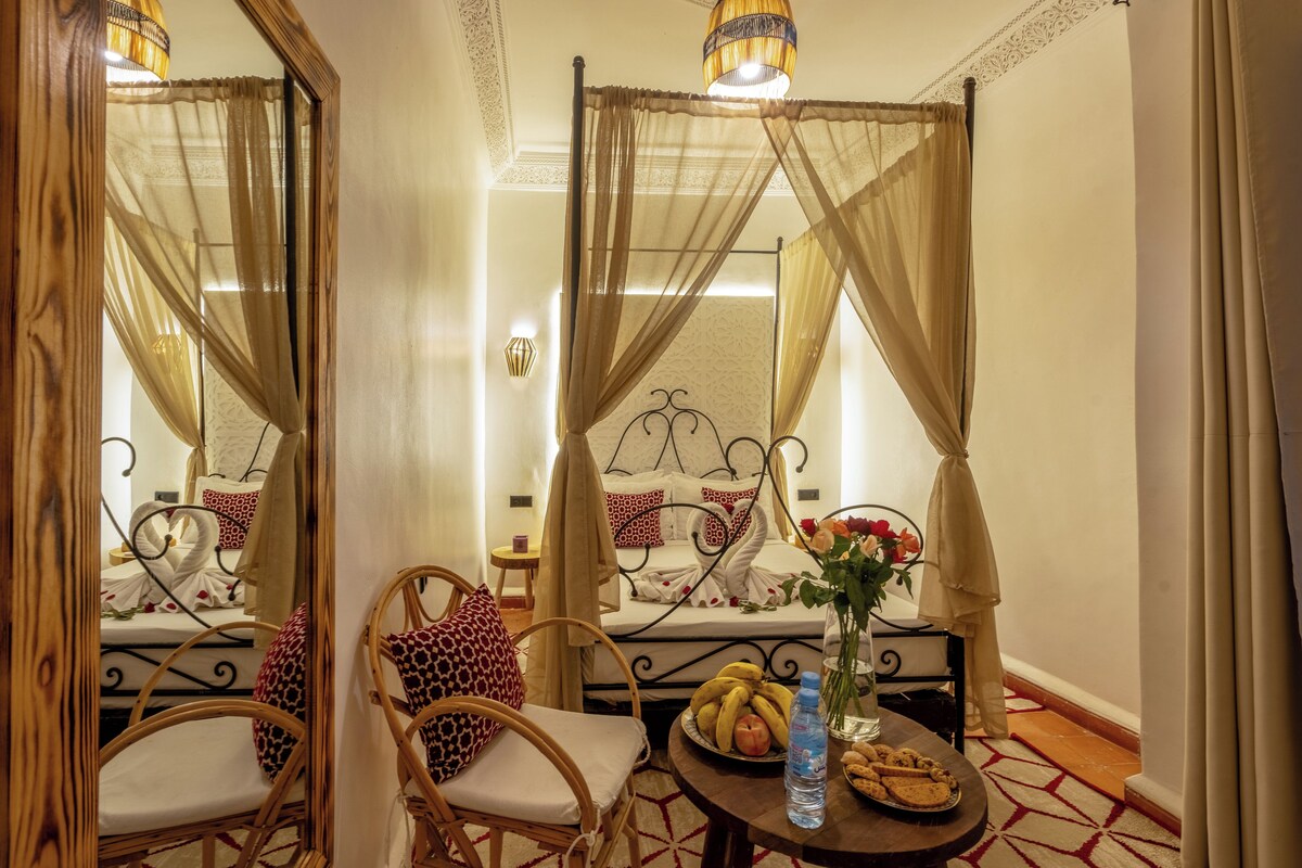 A room with a bed, a table with food, chairs, and a mirror.