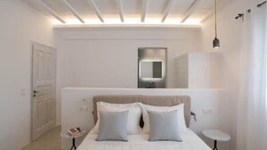 Een moderne slaapkamer met een groot bed, een nachtkastje, een klein rond tafeltje en een spiegel boven het bed.