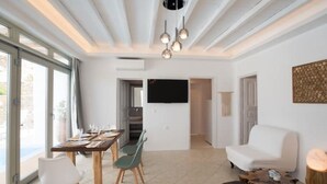 Een moderne woonkamer met een eethoek, een wandtelevisie en een groot raam dat voor natuurlijk licht zorgt.
