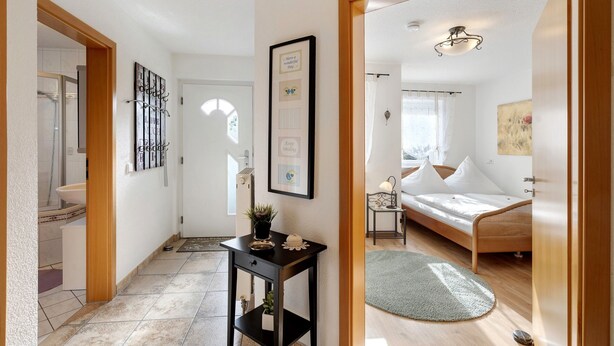 Ein Flur, der in ein Schlafzimmer mit einem Bett, einem Nachttisch und einem an der Wand befestigten Kunstwerk führt.