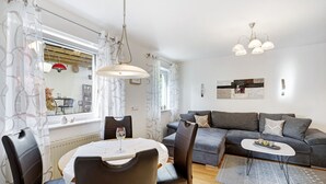 Ein modernes Wohnzimmer mit einer Couch, einem Esstisch mit Stühlen, einer Kandelaber und Blick ins Freie.