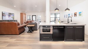 Een moderne keuken met een centraal eiland, een ingebouwde oven en een vaatwasser. Er is een eethoek met een tafel en stoelen, en een woonkamer met een bank en een televisie.