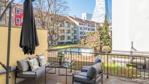 A balcony with outdoor furniture, a potted plant, and a view of a modern building and residential buildings in the background. - Special *Roger F. Rabbit 1* Apartment (Basel)