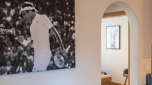 A room with a large poster of a tennis player, a framed picture of a rabbit, and a wooden chair. - Special *Roger F. Rabbit 1* Apartment (Basel)
