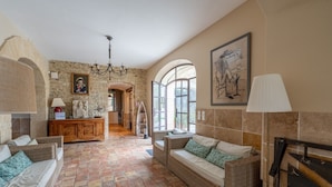 A spacious room with a stone wall, a chandelier, wicker furniture, and a large window.