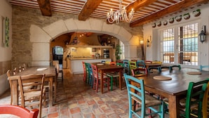 A rustic dining area with a stone archway, wooden tables, colorful chairs, and a chandelier.