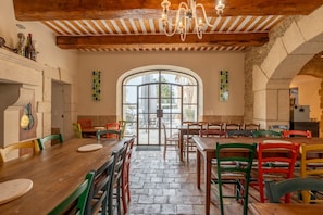 A dining area with wooden tables and chairs, a chandelier, and a large arched window.