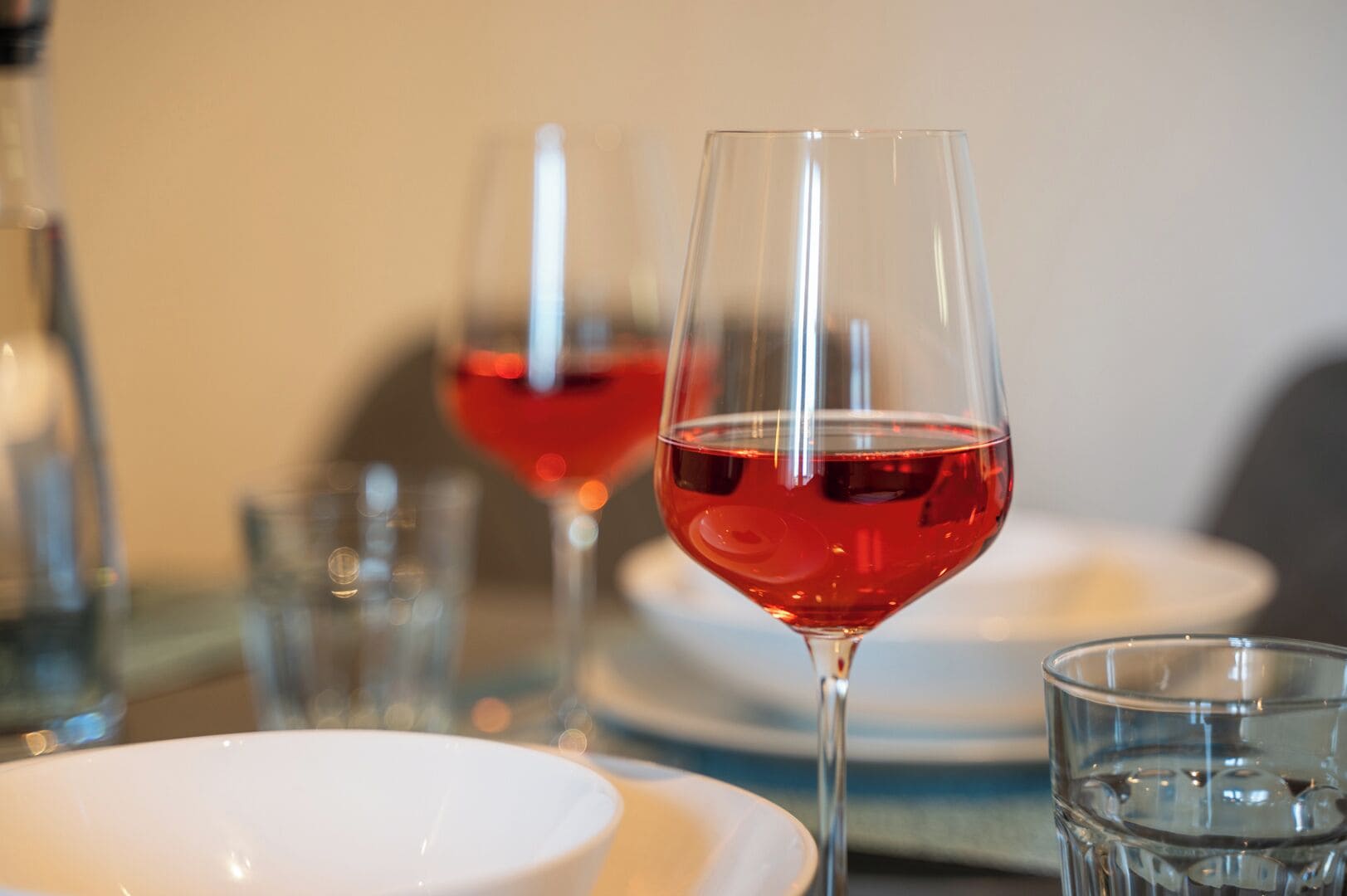A dining table with two wine glasses filled with red wine, a white plate, and a clear glass.