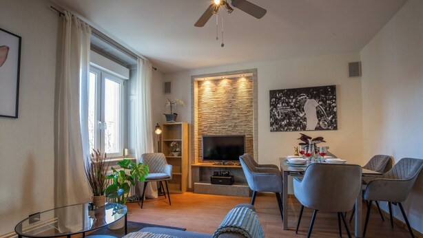A modern living room with a flat-screen TV, a dining area with a table set for two, and a seating area with a sofa and armchairs. - Special *Roger F. Rabbit 2* Apartment (Basel)
