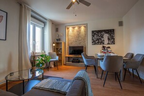 Un salon moderne doté d’un téléviseur à écran plat, d’un coin repas avec une table dressée pour deux personnes et d’un espace détente avec un canapé et des fauteuils.