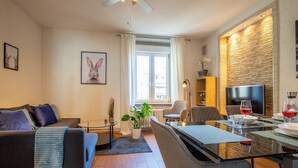 A modern living room with a sofa, armchairs, a dining table set for two, a television, and a large window with curtains. - Special *Roger F. Rabbit 2* Apartment (Basel)