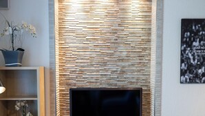 A modern living room with a flat-screen TV mounted on a textured wall, a built-in entertainment unit below, and a seating area with a blue chair. - Special *Roger F. Rabbit 2* Apartment (Basel)
